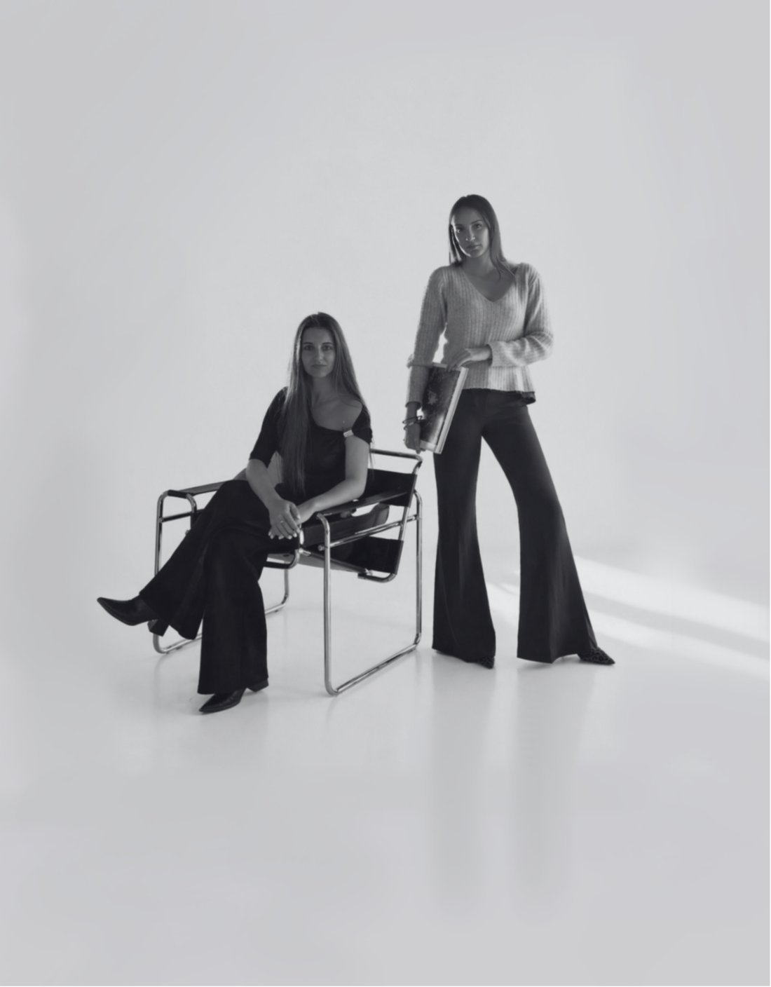 Retrato de las dos socias de Nítido Studio, una sentada y otra de pie, en un espacio blanco