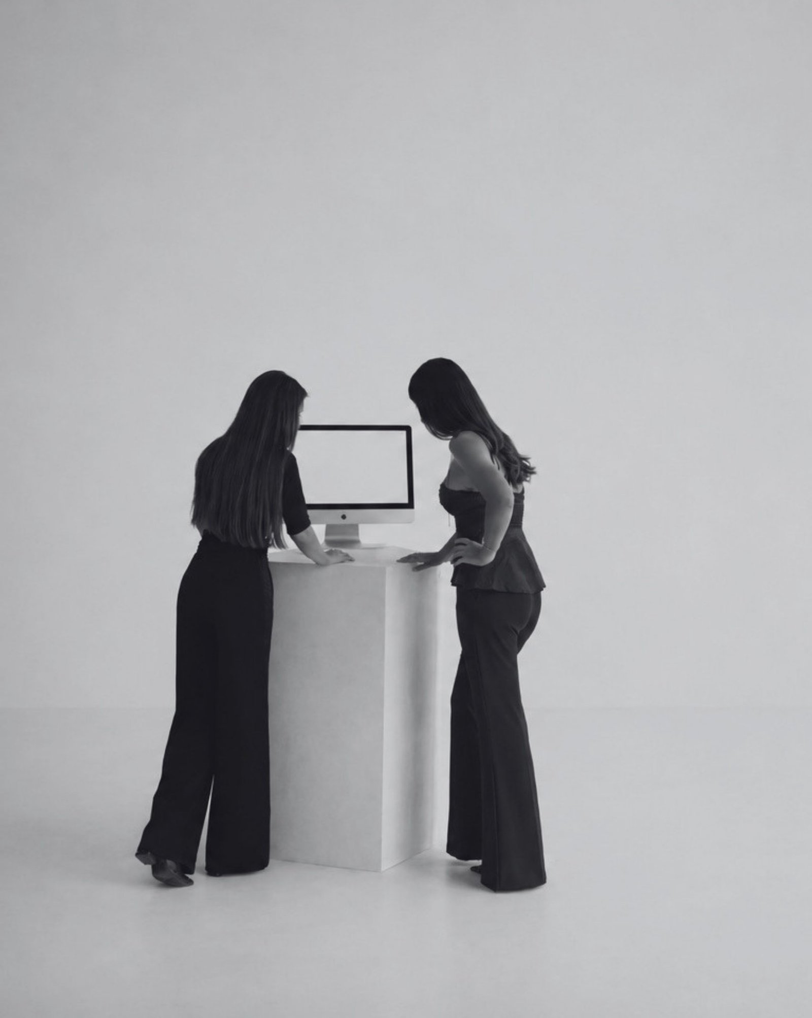 Las dos socias de Nítido Studio revisando un proyecto en pantalla, de pie ante un pedestal blanco